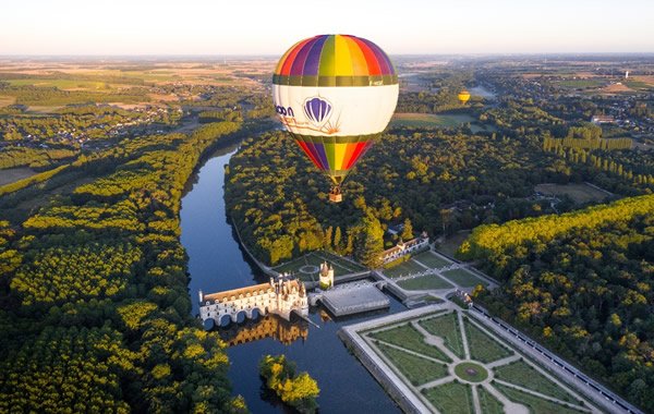 Montgolfière multicolore en vol au lever du soleil au dessus du château de Chenonceau et du Cher